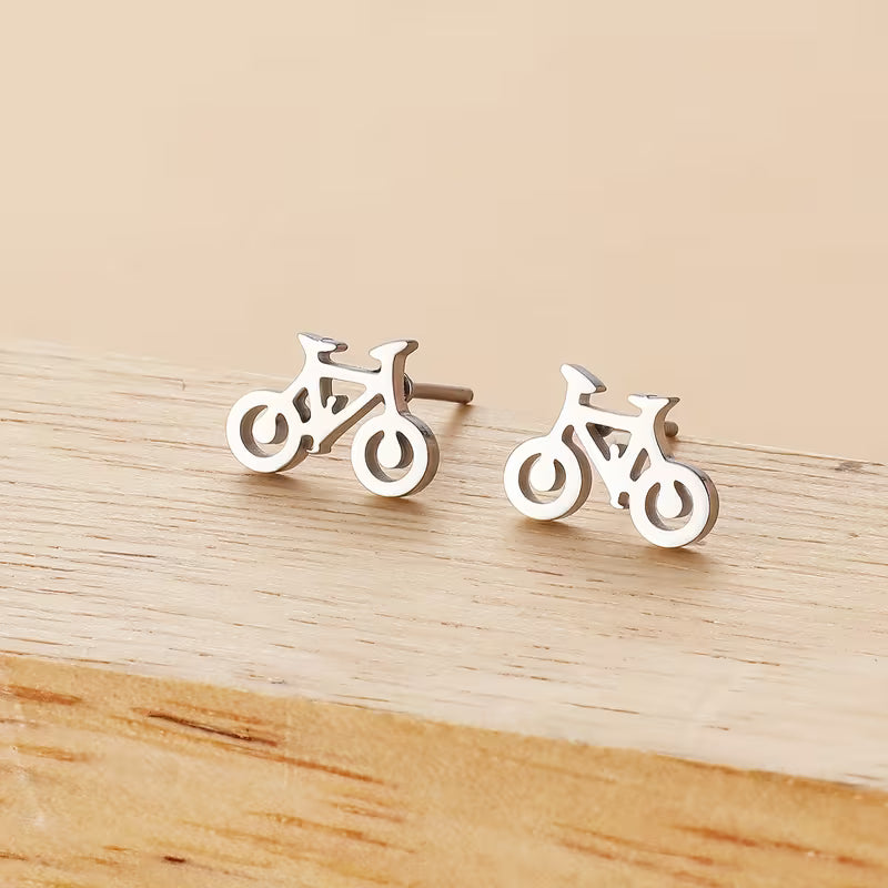 Silver bicycle-shaped stud earrings on a wooden surface